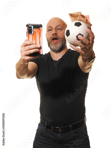 Obraz na płótnie Betting on soccer or football concept. Adult male gambler in black shirt in his 50s holding ball and cash and phone, model with grey beard on white background. Making money on sport events concept. w salonie