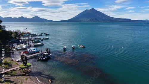 Beautiful cinematic aerial view os the Panajachel town surrounded by Toliman and Atitlan volcanoes, next to the Atitlan lake its piers and traditional fisher and tourist boats - Guatemala