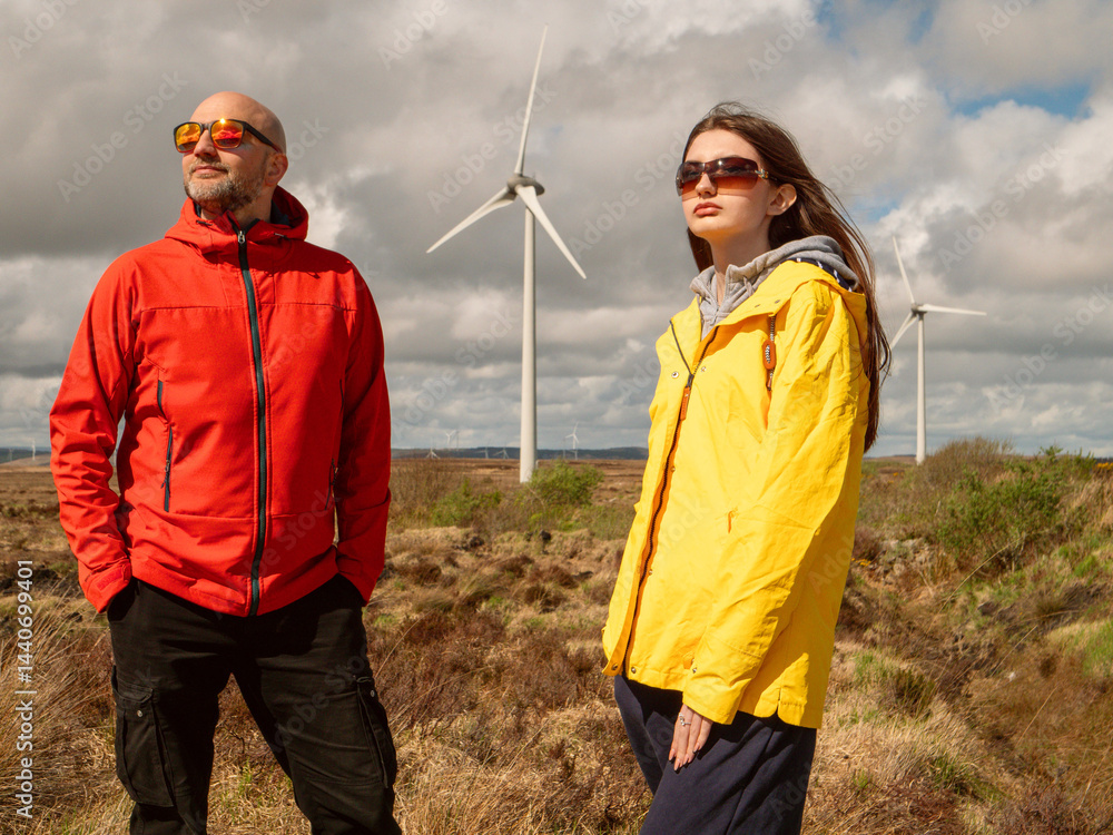 Father in red jacket and daughter in yellow enjoy warm sunny day. Wind turbine and huge wild field and cloudy sky in the background. Divorced man day with his daughter concept. Outdoor activity.