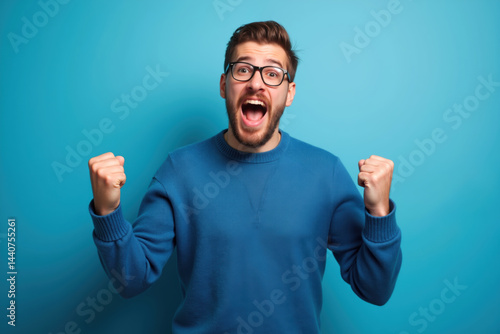 A man wearing glasses and a blue sweater celebrates with raised fists and an open mouth.