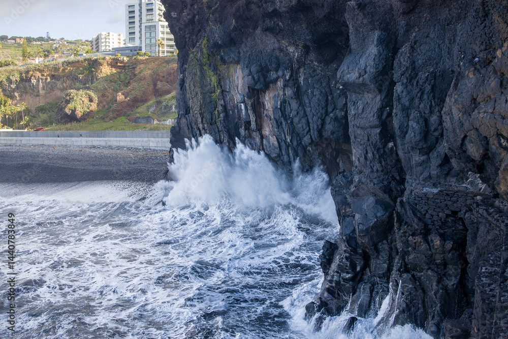 Waves crashing against volcanic cliffs in Madeira near urban development