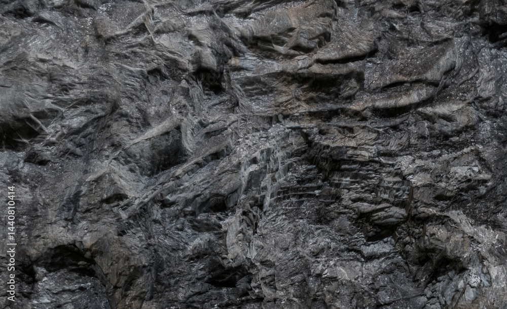 Dark, textured rock face. Close-up view of rough, layered geological formation Dark, textured rock face. Close-up view of rough, layered geological formation