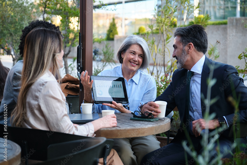 Business team having a meeting at an outdoor cafe, analyzing data on a tablet and discussing strategy