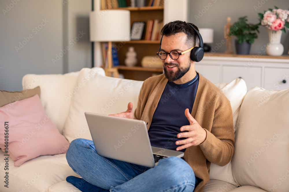 Bearded Professional In Casual Attire Using Laptop And Headphones While Working Remotely From Cozy Home Environment Bearded Professional In Casual Attire Using Laptop And Headphones While Working Remotely From Cozy Home Environment