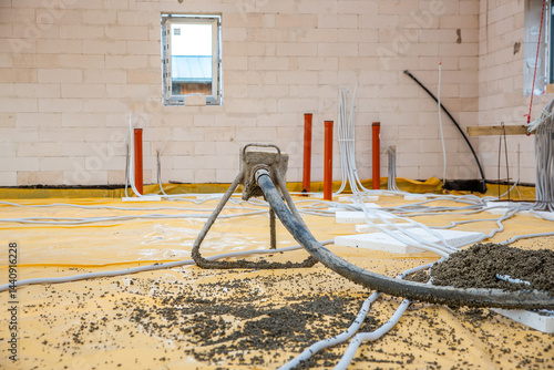 Obraz na płótnie Interior under construction with brick walls, a concrete hose pouring onto a yellow sheet, and visible pipes and conduits on the floor. w salonie