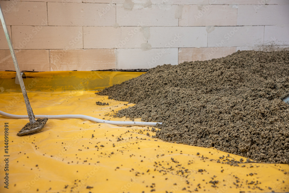 Partially finished interior with a white brick wall, yellow protective sheet on the floor, loose aggregate material, and tools for flooring work.