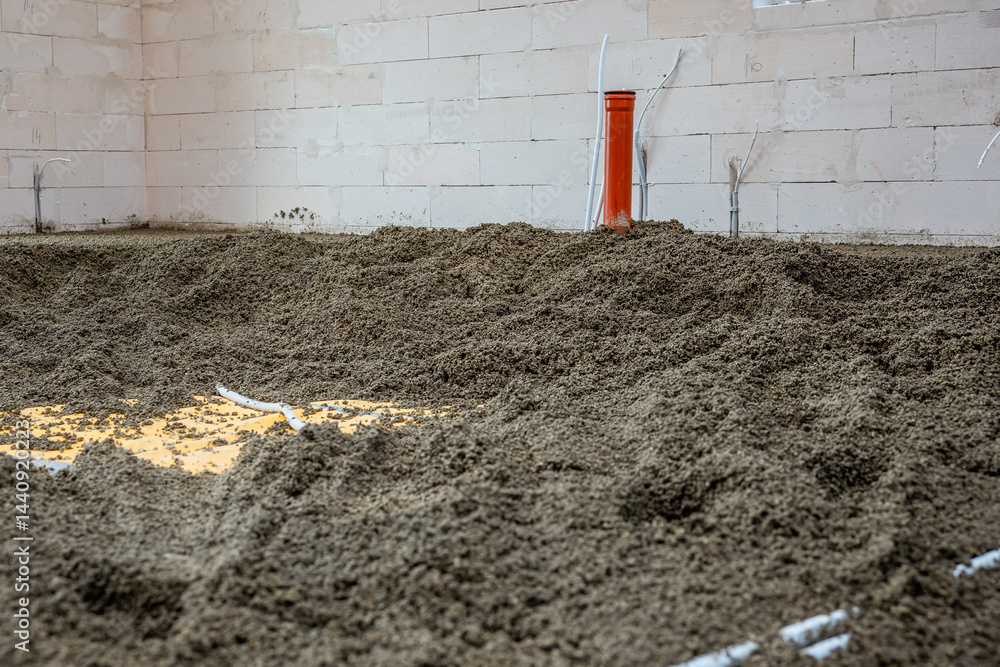 Interior of a construction site featuring an orange vertical pipe, white conduit pipes, loose gravel floor, and light colored concrete block walls.