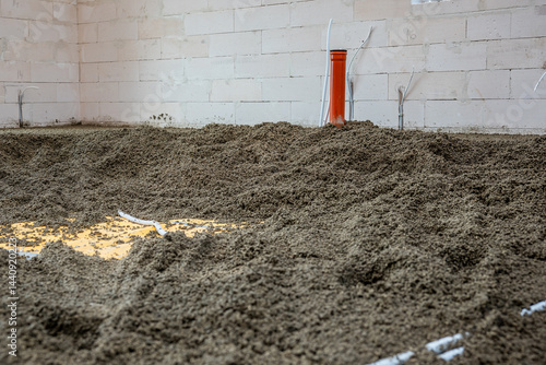 Obraz na płótnie Interior of a construction site featuring an orange vertical pipe, white conduit pipes, loose gravel floor, and light colored concrete block walls. w salonie