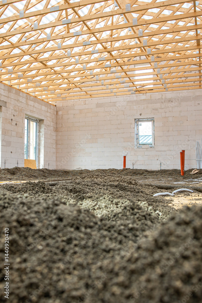Interior of a building under construction with white brick walls, exposed wooden truss roof, loose soil floor, and visible utility pipes.