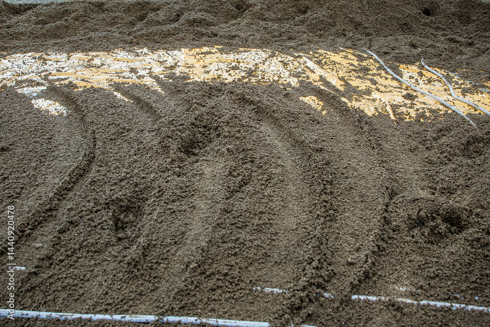 A detailed view of wet cement or sand with grooves, exposed yellow material, and embedded white pipes, indicating a construction process.