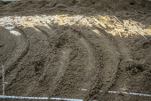 A detailed view of wet cement or sand with grooves, exposed yellow material, and embedded white pipes, indicating a construction process.