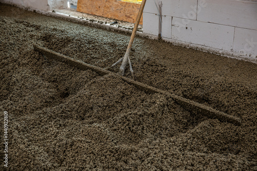 Obraz na płótnie An indoor construction site shows wet concrete being leveled with a rake like tool. Unfinished white block walls and a wooden panel are visible. w salonie