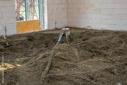 Obraz na płótnie White brick walls and an unfinished floor being leveled with concrete. A hose distributes material, with light entering through a window opening. w salonie