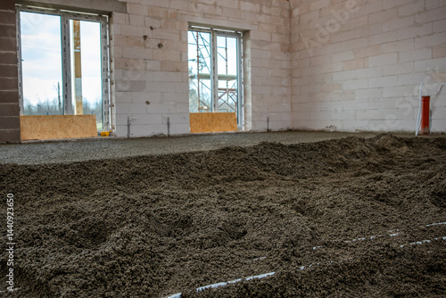 Interior space under construction featuring white brick walls, concrete floor, large window openings, scaffolding, and a red utility pipe on the right.