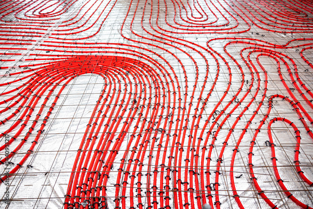 Detailed view of red underfloor heating pipes secured to a metal grid, arranged in a curved pattern on a construction surface for concrete pouring.