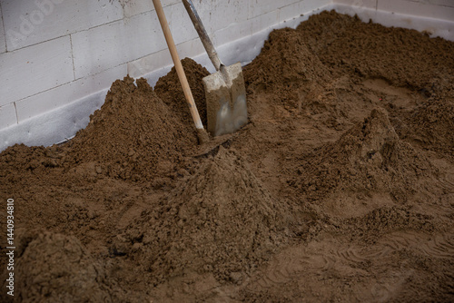 Obraz na płótnie Interior of a construction site with sand spread on the floor, tools against a white brick wall, and visible marks indicating active preparation work. w salonie