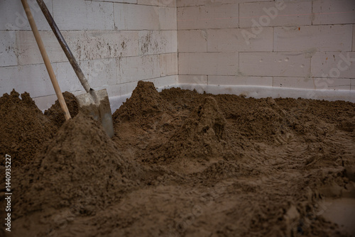 Obraz na płótnie Interior of a construction site with sand piles on the floor, a shovel against white block walls, and visible signs of ongoing work. w salonie