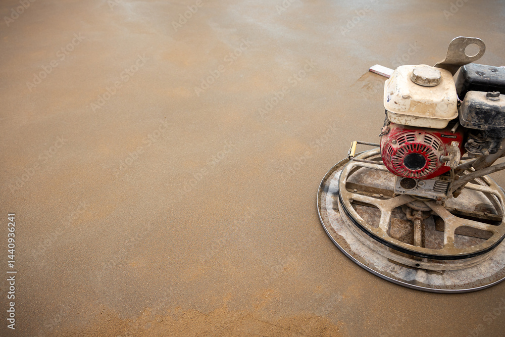 A power trowel with a red engine rests on a damp, even concrete floor, recently smoothed and finished at a construction site.