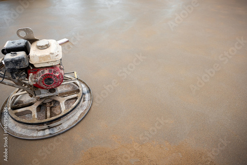 Obraz na płótnie A power trowel machine with a red and white motor smooths a wet concrete surface. The circular blade contacts the floor, showing drying patches. w salonie