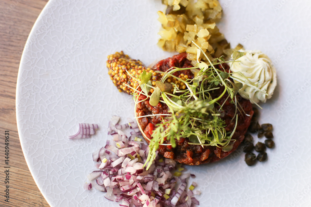 Beef tartare served with onion. Mustard and pickles. Gourmet starter. Traditional meat dish. Fine dining presentation. Fresh herbs decoration. Elegant restaurant appetizer.
