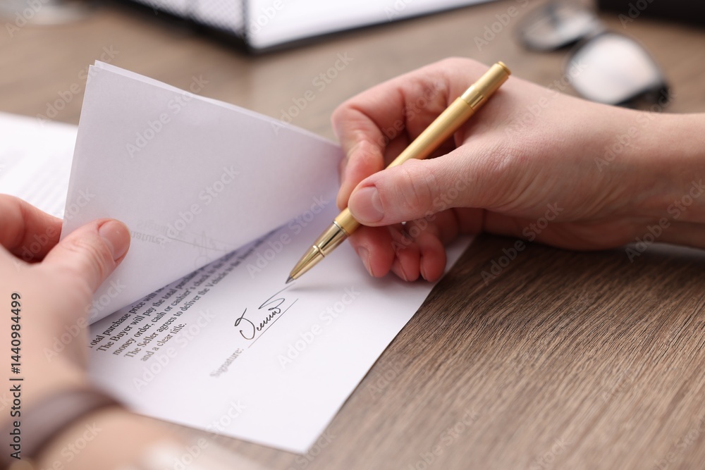Woman putting signature on document at wooden table, closeup Woman putting signature on document at wooden table, closeup