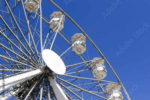White ferris wheel against blue sky. Bright sunny day. Modern amusement ride. Fun outdoor attraction. Giant observation wheel. Minimalist fairground scene. Holiday and leisure concept.