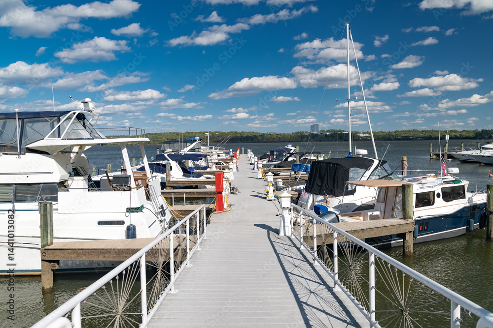 Fototapeta premium Wooden pier walkway leading to boats and yachts moored at the marina in Annapolis, Maryland. Blue sky with clouds.
