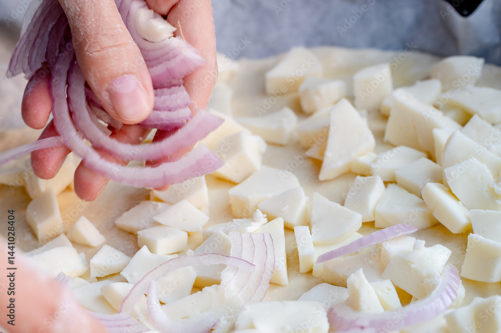 Close-up scene of female hands. Adding onion to dough on kitchen countertop. Making homemade pizza with three types of cheese – female hands in action.