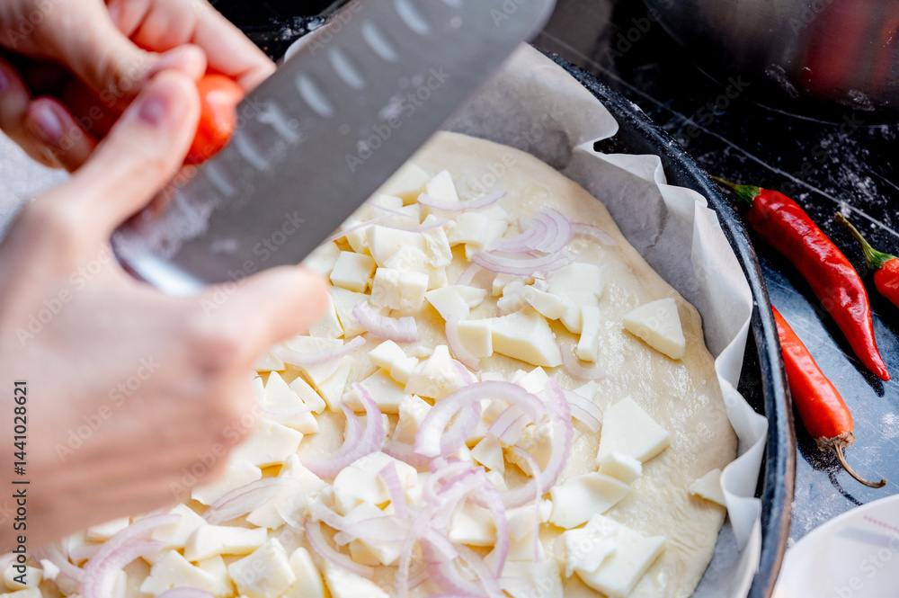 Close-up scene of female hands. Cutting tomato adding pieces of fresh tomato to dough on kitchen countertop. Making homemade pizza with three types of cheese – female hands in action.
