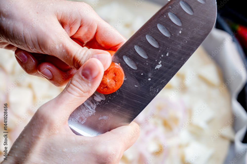 Close-up scene of female hands. Cutting tomato adding pieces of fresh tomato to dough on kitchen countertop. Making homemade pizza with three types of cheese – female hands in action.