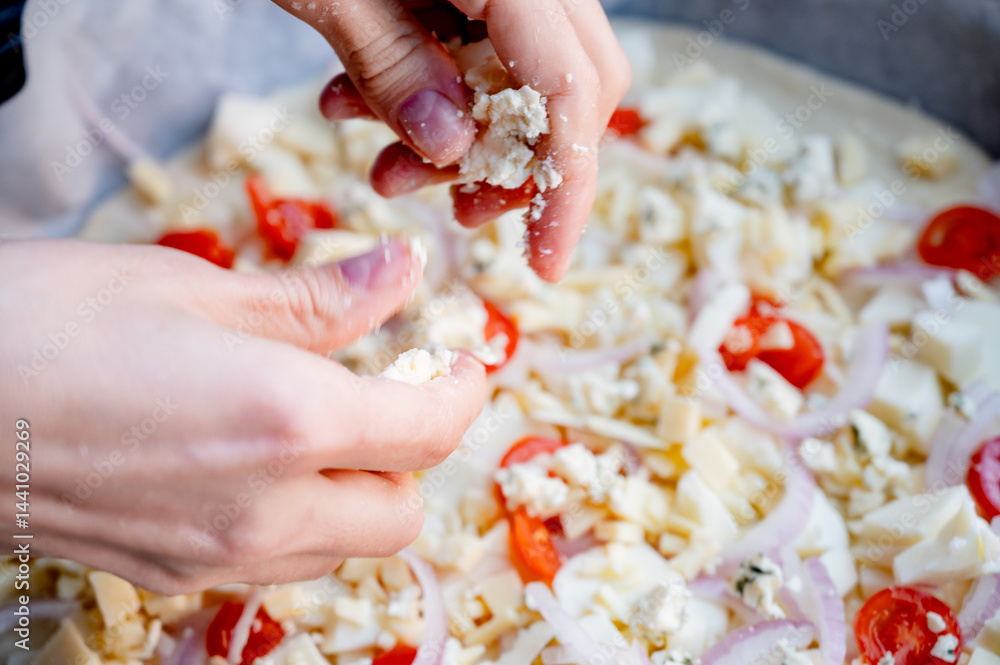 Close-up scene of female hands. Adding a mixture of three cheeses - mozzarella, parmesan and gorgonzola to the dough on the kitchen countertop. Making homemade pizza with three types of cheese - femal
