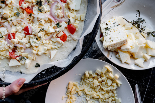 Obraz na płótnie A homemade pizza in its raw form, assembled with toppings. The dough is uncooked but fully prepared with sauce, cheese, and fresh ingredients. The kitchen is cozy and softly lit, with utensils, bowls, w salonie