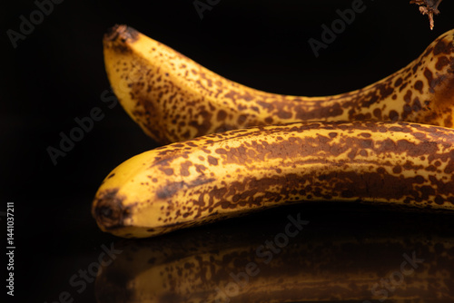 Ripe banana, almost overripe bananas on a black reflective surface and dark background, selective focus.