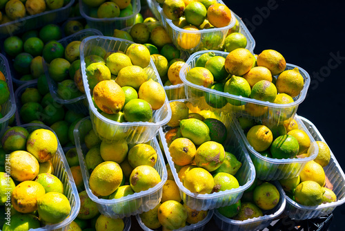 Obraz na płótnie Vibrant assortment of lemons and limes packed closely in plastic containers, highlighting their contrasting yellow and green. Stacked containers overflowing with ripe citrus fruits at street market w salonie