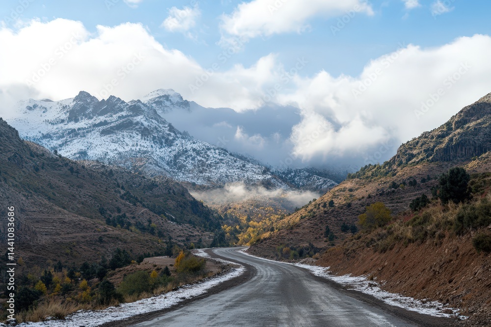 Fototapeta premium Winding Road Through Snowy Mountain Pass with Dramatic Cloudy Sky