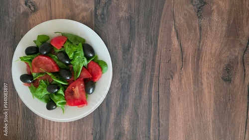 Fresh salad with spinach, tomatoes, olives, and soy sauce on a rustic wooden table. Healthy, light meal. Top view, copy space. Delicious vegetarian appetizer.