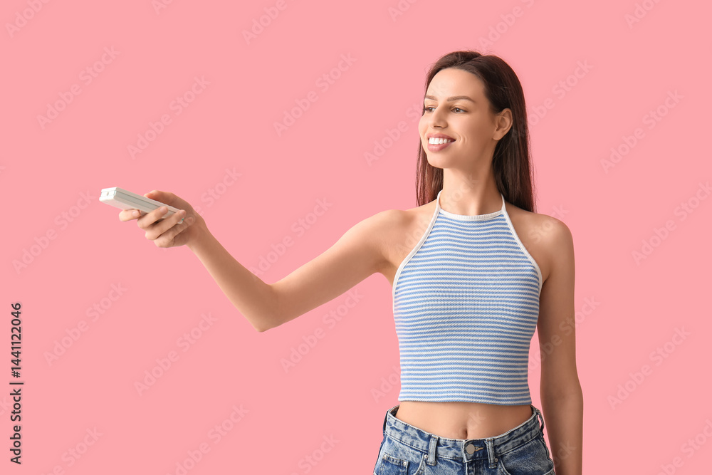 Young woman with air conditioner remote control on pink background