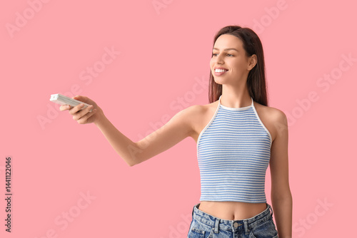 Obraz na płótnie Young woman with air conditioner remote control on pink background w salonie
