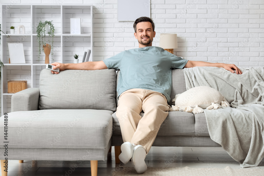 Handsome young man resting on sofa with operating air conditioner in living room Handsome young man resting on sofa with operating air conditioner in living room
