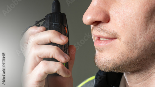 Close-up of a worker speaking into a handheld radio during site operations, wearing safety gear. Activity: Construction, Security, Site Management.
