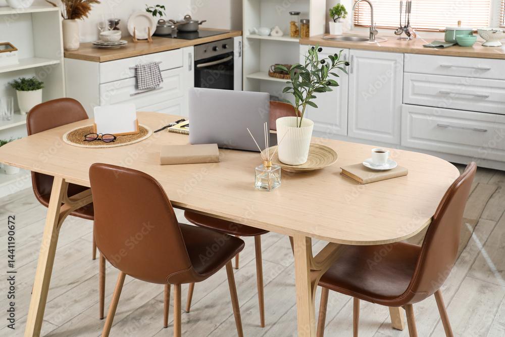 Interior of light kitchen with laptop on dining table, counters and plants Interior of light kitchen with laptop on dining table, counters and plants