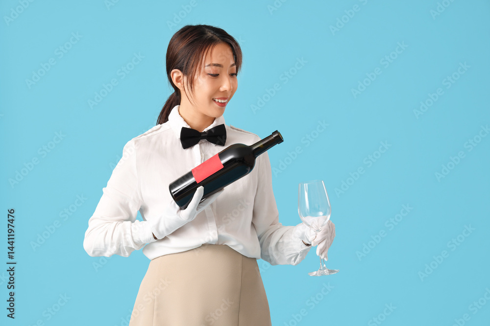 Young Asian smiling waitress with bottle of wine and glass on blue background Young Asian smiling waitress with bottle of wine and glass on blue background