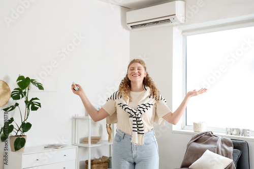 Obraz na płótnie Beautiful smiling woman switching on air conditioner in living room w salonie