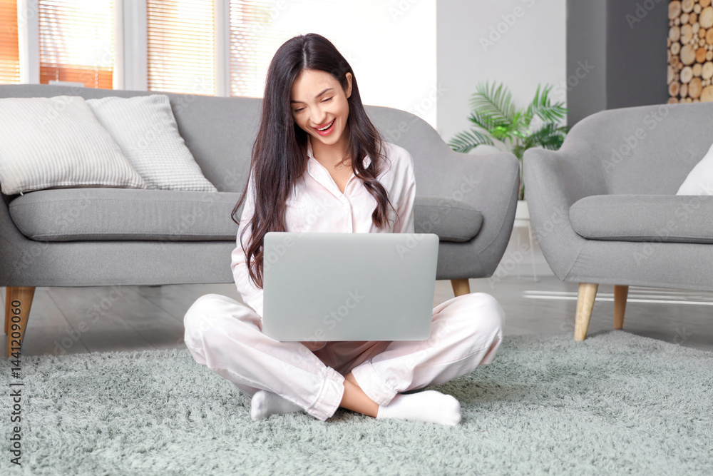 Female freelancer in pink pajamas working with laptop on carpet at home Female freelancer in pink pajamas working with laptop on carpet at home