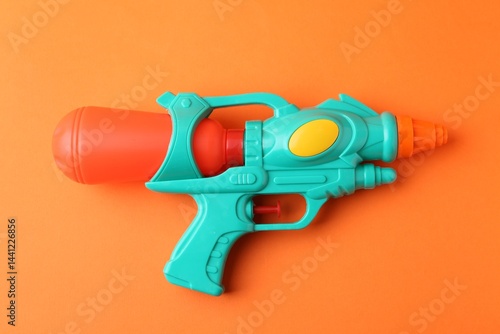 Bright plastic water gun on orange background, top view