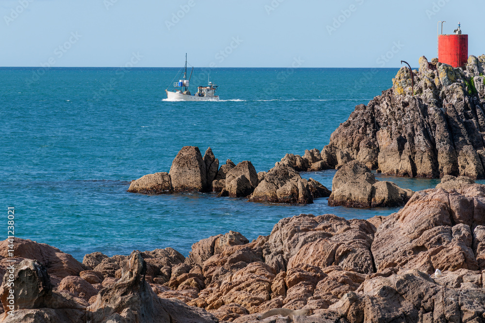 Fishing boat motors past red beacon of North Rock at base Mount Maunganui
