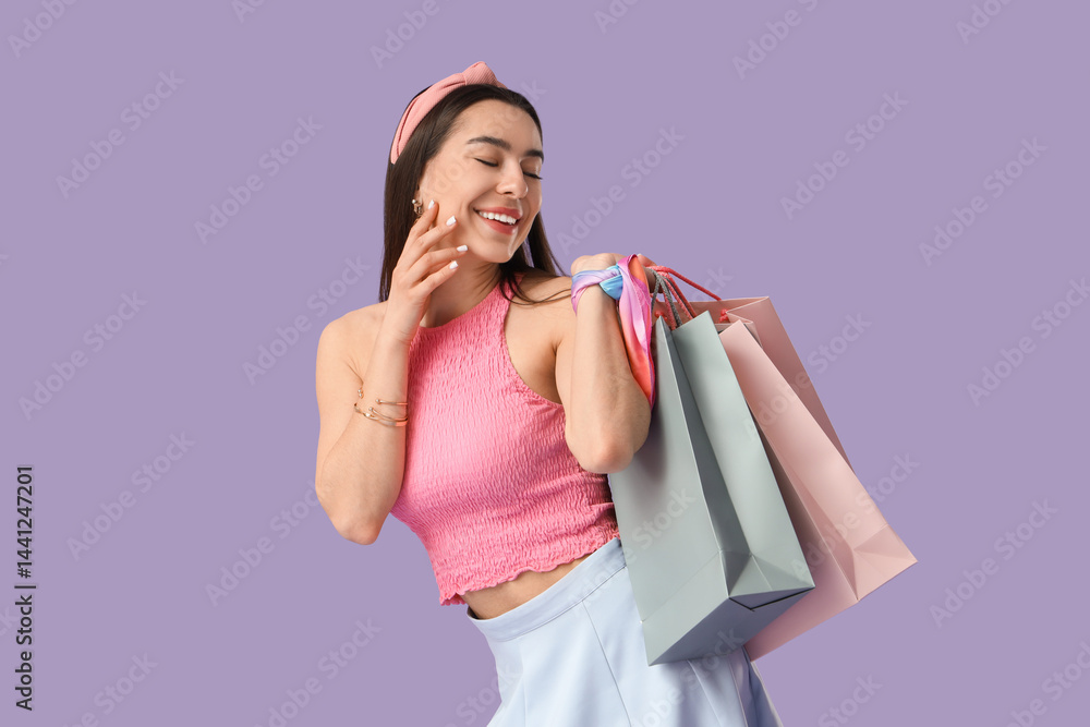 Happy young woman with shopping bags on lilac background