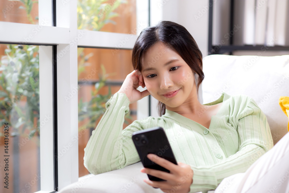 Young asian businesswoman looking smartphone smiling and relax sitting on sofa in living room at home, cheerful woman watching smart phone sitting on couch in home, lifestyle and communication. Young asian businesswoman looking smartphone smiling and relax sitting on sofa in living room at home, cheerful woman watching smart phone sitting on couch in home, lifestyle and communication.