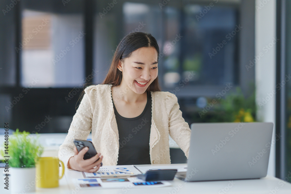 Young happy businesswoman using laptop and smartphone while working at her desk in modern office Young happy businesswoman using laptop and smartphone while working at her desk in modern office