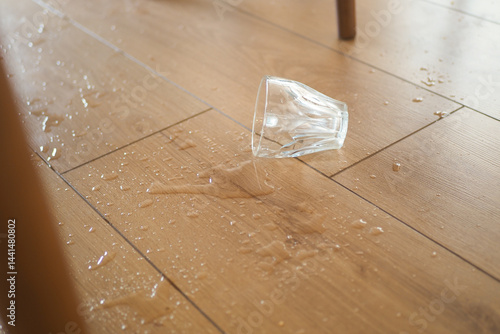 Glass tipped over spilling water on wooden floor during daytime